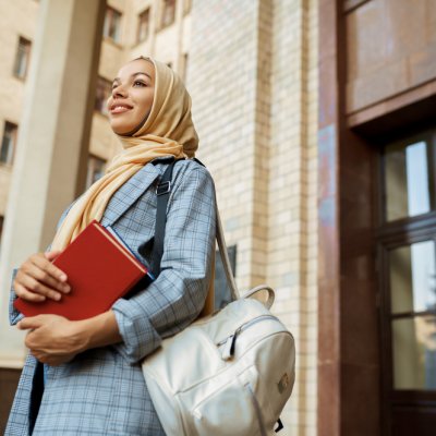 Arab woman wearing hijab standing by university entrance 
